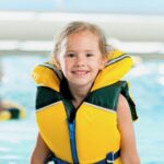 A young girl in a bright life jacket plays in a pool